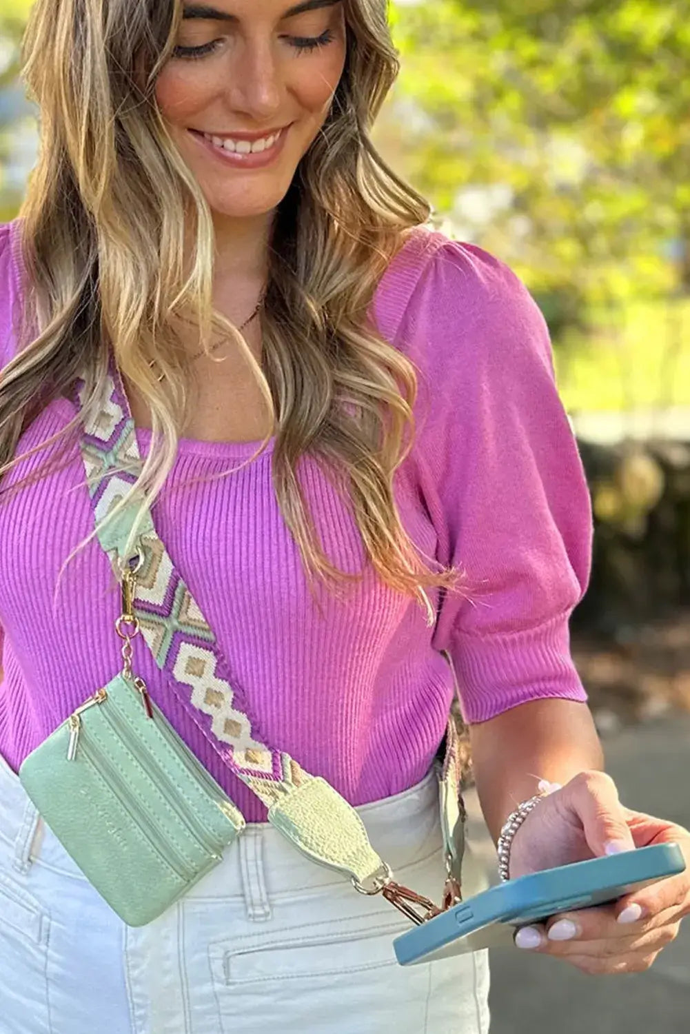 Model wearing HANDS FREE HARMONY CROSSBODY in mint green with geometric strap, checking phone outdoors.