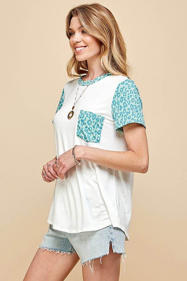 Woman wearing a SPOT OF STYLE TEE with turquoise leopard print sleeves and pocket, styled casually with denim shorts.