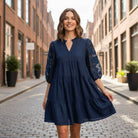 DEEP SEA DREAMS DRESS  Umgee worn by a smiling woman in a navy tiered dress with floral sleeves, walking in a city street.