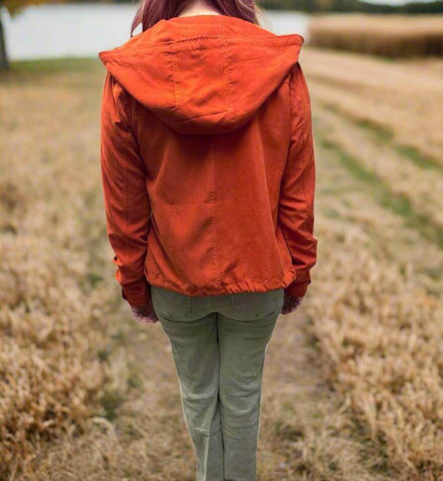 Woman wearing Autumn Sunrise Jacket in ginger color, walking through a field during fall.