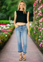 Model wearing JUDY BLUE Amelia Jeans with a cropped top amidst colorful flowers, showcasing a stylish midrise bootcut fit.