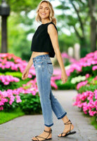 Woman in cropped top wearing JUDY BLUE Amelia Jeans, enjoying a sunny day in a floral garden.