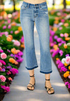 Model wearing Judy Blue Amelia cropped bootcut jeans in a floral garden, showcasing stretchy fit and release hem.