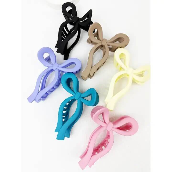 Six colorful bow-shaped hair clips in Taupe Cocoa, Jett Black, Candy Pink, Dark Teal, Violet Purple, and Lemon Cream.