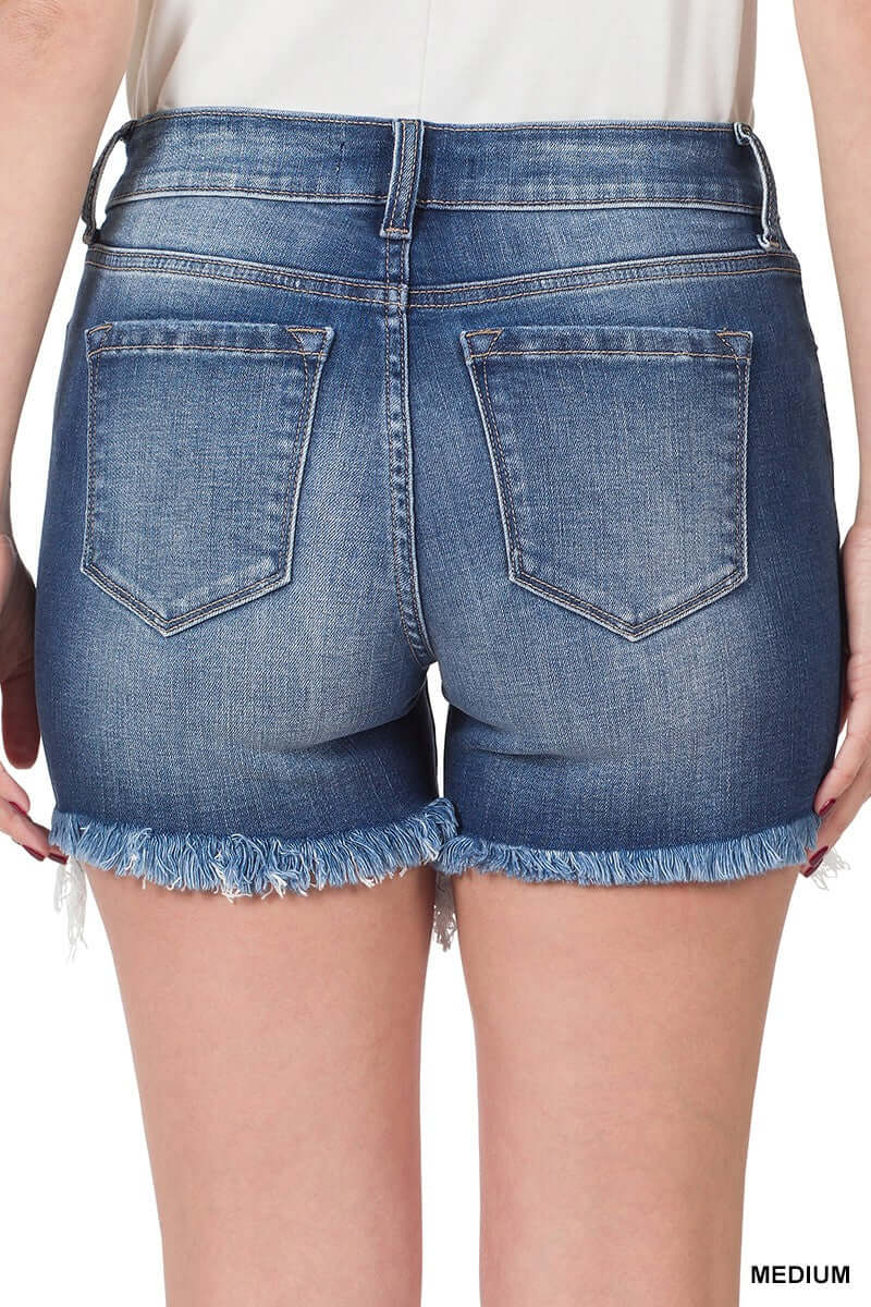 Back view of medium wash denim shorts with frayed hem, showcasing stretchy fit and mid-rise design.