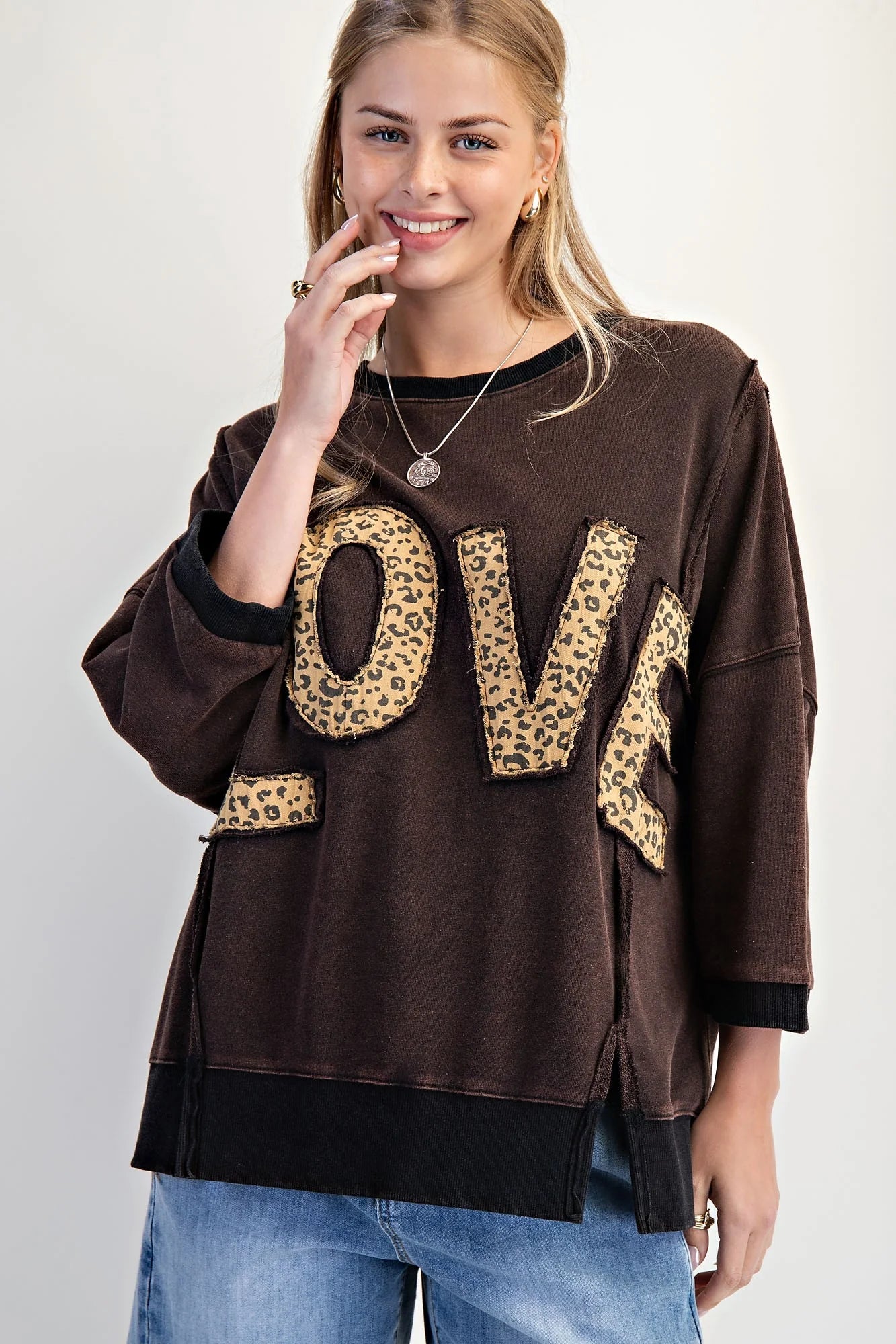 LOVE UNTAMED TOP - Easel model wearing dark wash oversized top with leopard patch letters, smiling and posing.