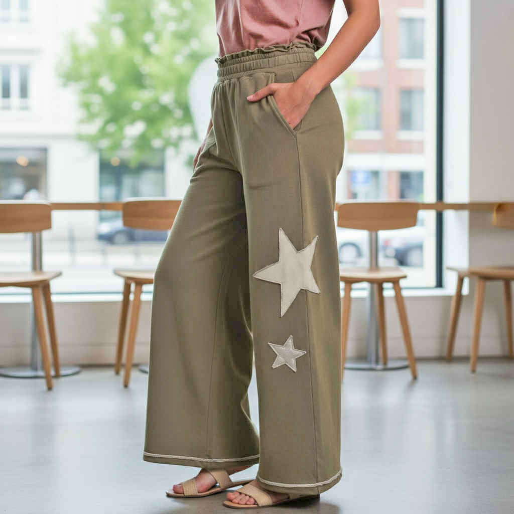 Stylish model wearing STARLIGHT STROLL PANTS UMGEE with star patch detailing in a trendy café setting.