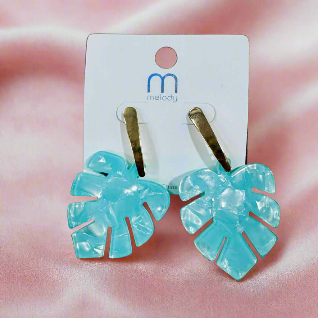 Aqua Palm Parade Earrings by Melody featuring monstera leaf design with gold-tone posts on a soft pink background.