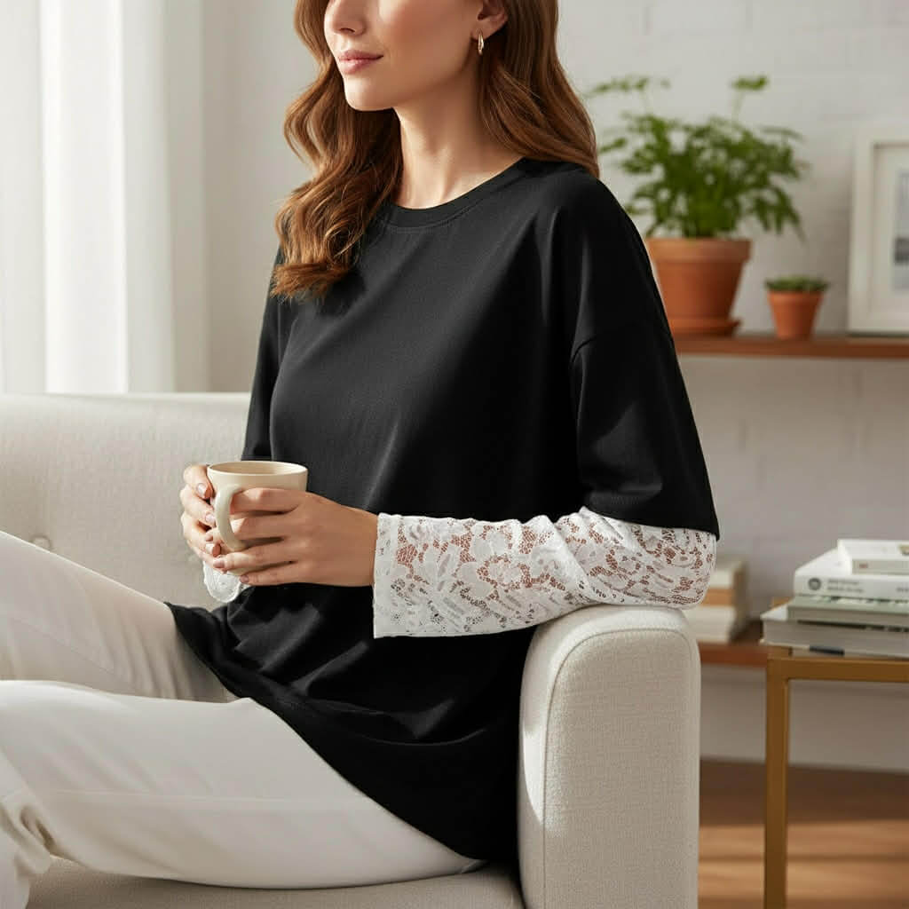 Woman wearing a COFFEE & CREAM TOP black tee with lace sleeves, relaxing with a cup of coffee.