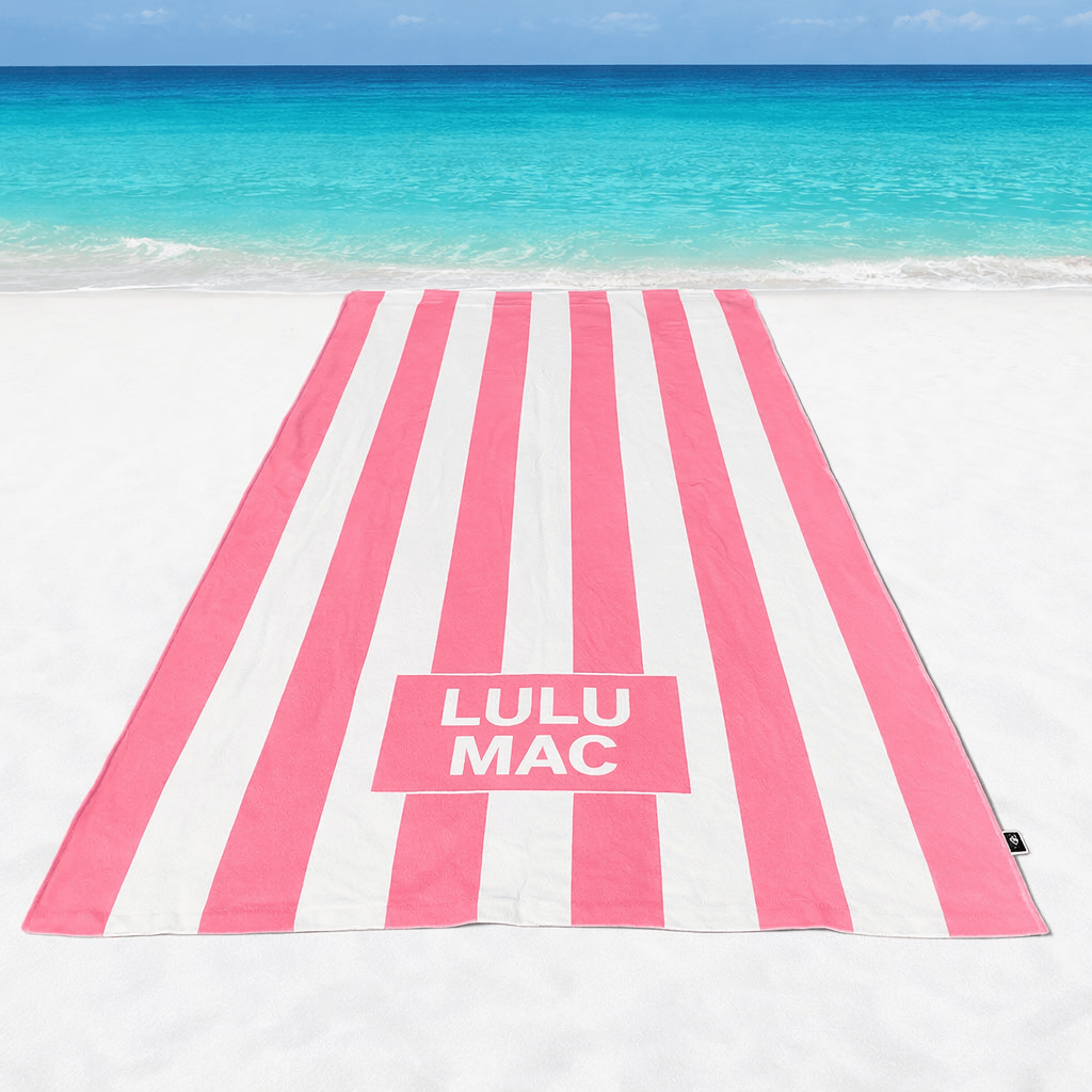 LULU MAC DARBY BEACH TOWEL (taffy pink) on the beach with turquoise water backdrop, extra-large striped design.