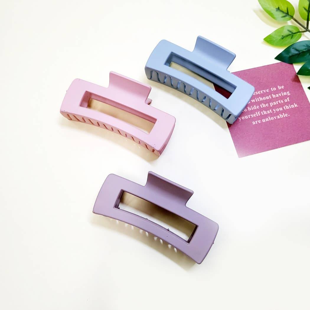 Large Chic Simplicity claw clips in pastel pink, blue, and lavender on a flat surface with greenery.