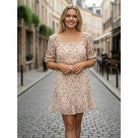 RUSTIC GRACE by Trixxi, model wearing soft orange floral mini dress in a charming street setting.