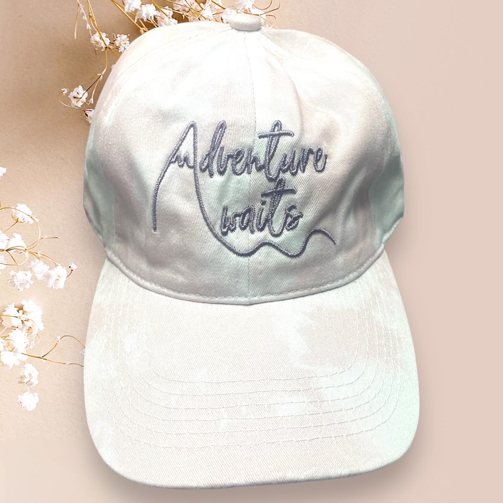 Distressed white Katydid baseball cap with 'Adventure Awaits' embroidery for retro flair. Perfect for casual outings.