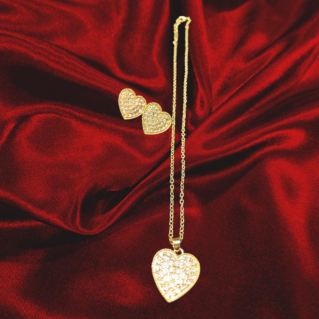 Gold heart-shaped earrings and necklace set sparkling on red satin fabric, perfect for love-themed occasions.