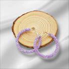 Violet Sparkle hoop earrings on a wooden slice, showcasing stunning purple hues for a chic look.