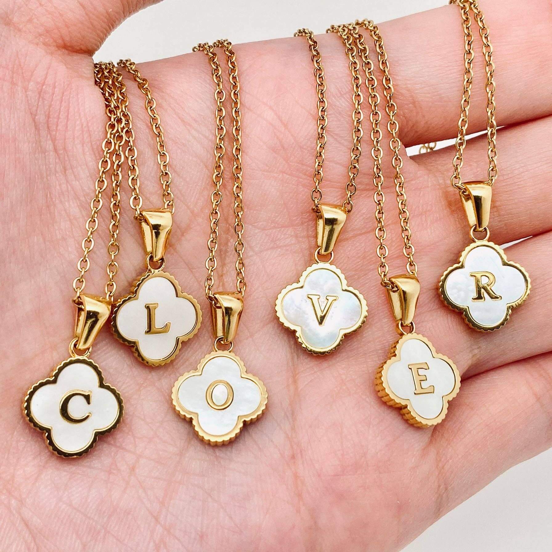 Close-up of MONOGRAM MOMENTS NECKLACE pendants, featuring gold frames and white enamel letters spelling 'CLOVER'.