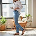 Woman wearing JUDY BLUE - AVERY JEANS in a bright living room, holding a coffee cup, styled for casual elegance.