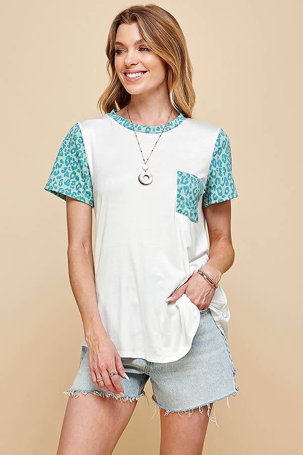 Woman wearing SPOT OF STYLE TEE with turquoise leopard print sleeves and pocket, paired with distressed denim shorts.