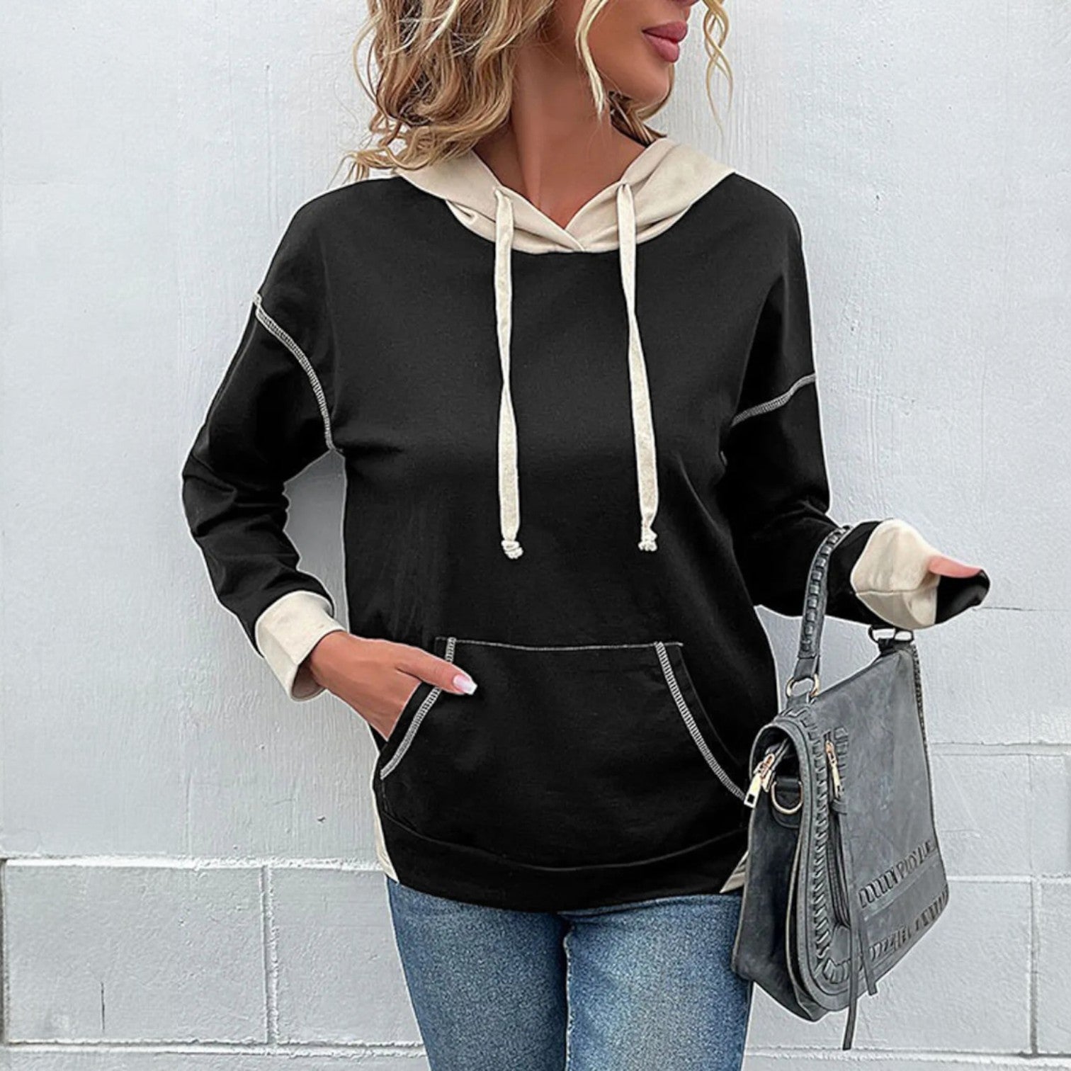 Woman wearing a MODERN EDGE HOODIE with contrast seams, paired with jeans and a stylish handbag for a casual look.