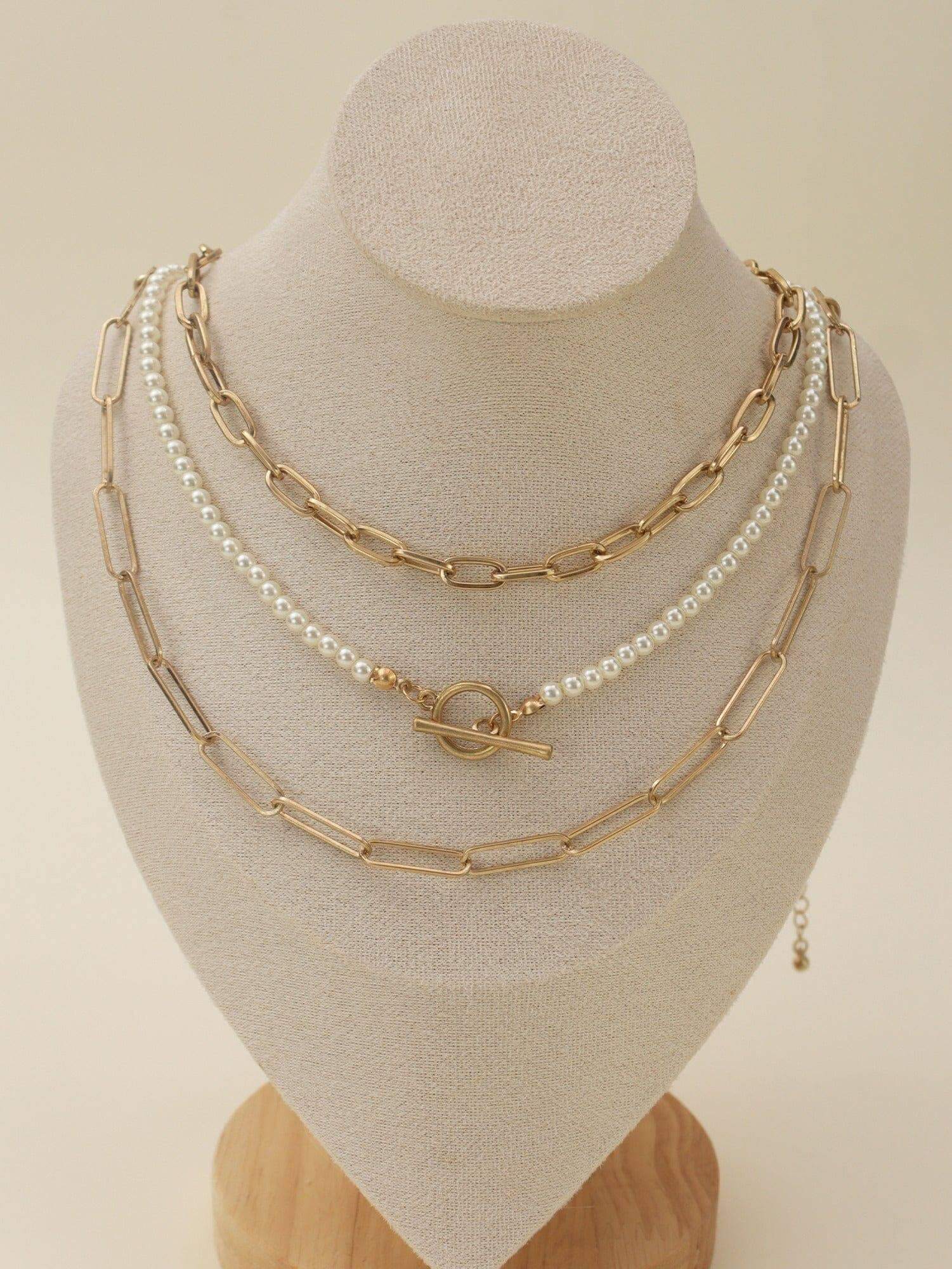 Serene Strands Necklace Set featuring gold and pearl layered necklaces displayed elegantly on a jewelry stand.