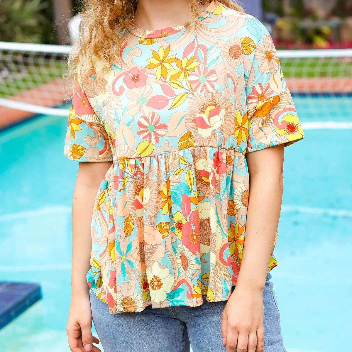 Model wearing the Retro Romance Top by Haptics, showcasing floral print and peplum silhouette by a pool.