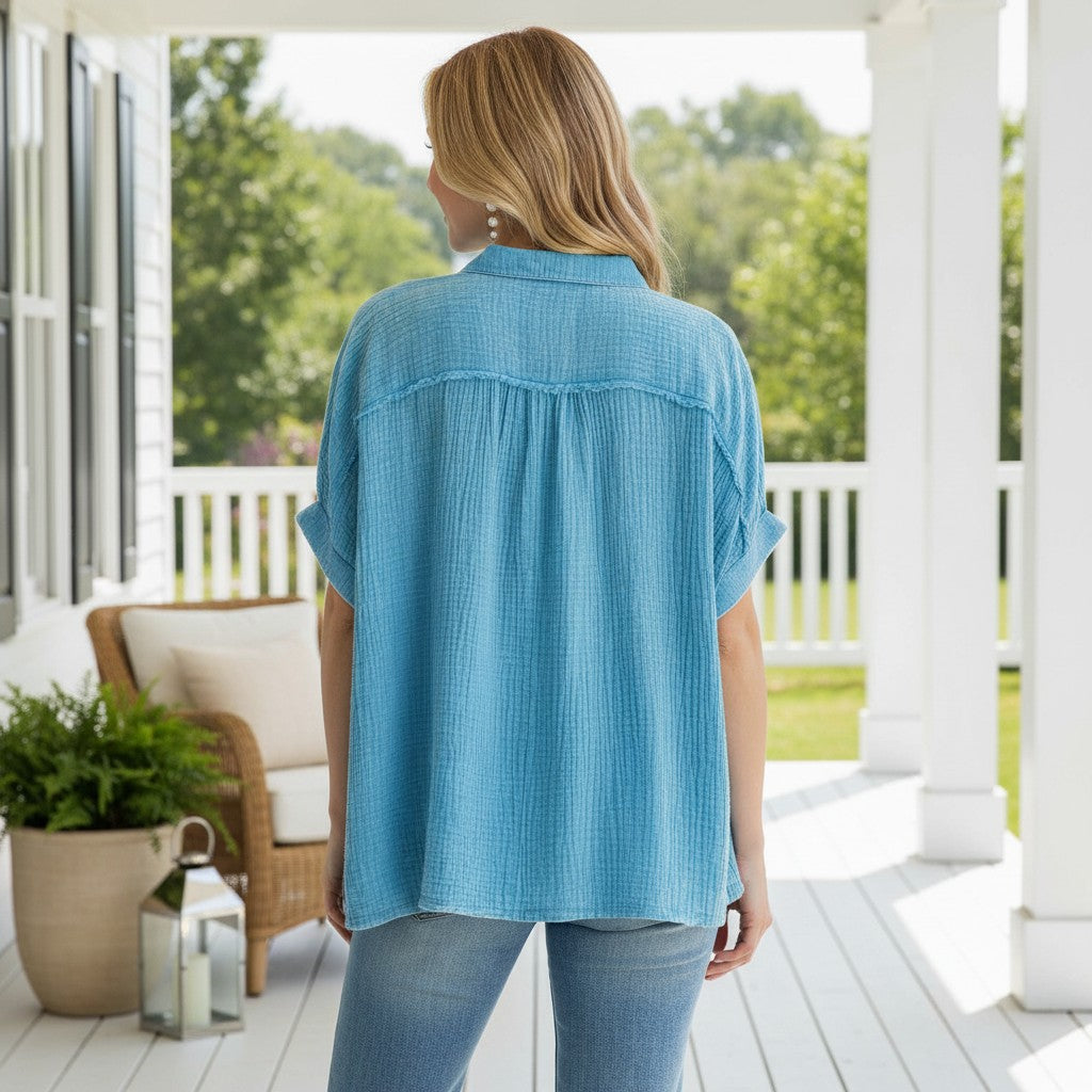 Back view of the CALMING COAST TOP - Umgee in light blue cotton gauze, showcasing its relaxed silhouette on a porch.