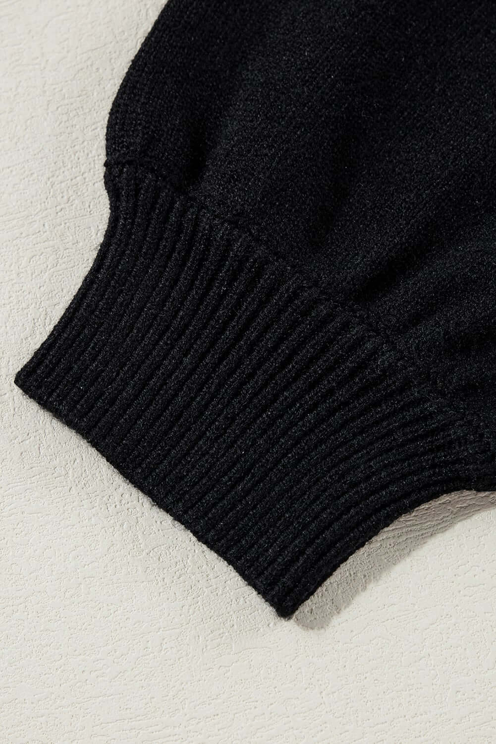 Close-up of the cuff of the MERRY & BRIGHT sweater by Vivian-Lu, showcasing ribbed black knit detail.
