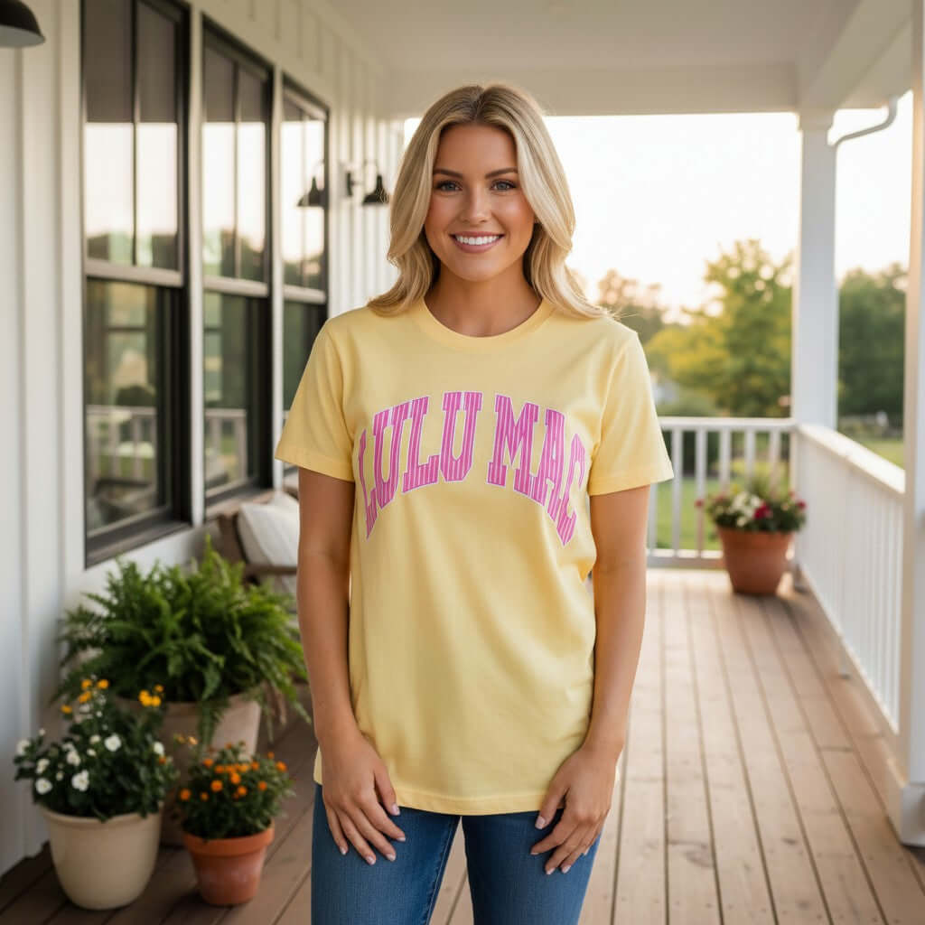 Model wearing LULU MAC BUTTER & PINK STRIPES COMFORT COLOR TEE in yellow with pink lettering on a porch.