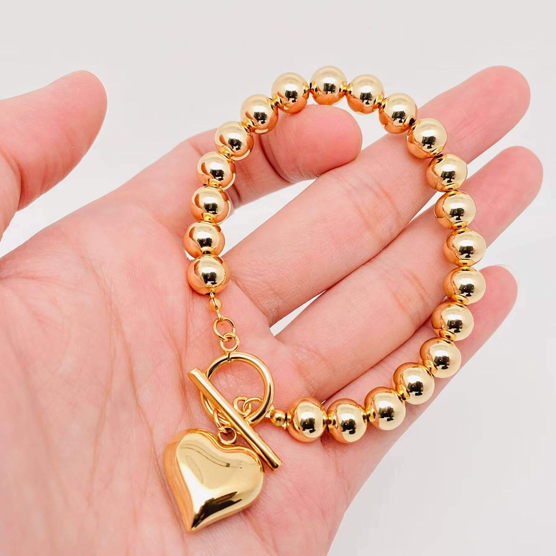 HEART OF GOLD BRACELET featuring polished gold beads and a heart charm on a hand.
