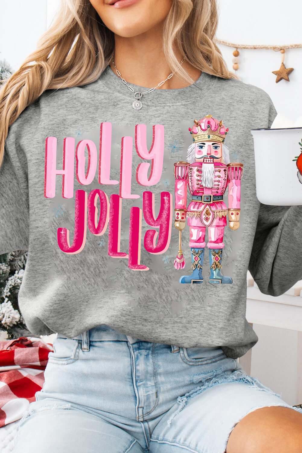 Model wearing a grey Christmas sweatshirt with 'HOLLY JOLLY' print and a nutcracker design.