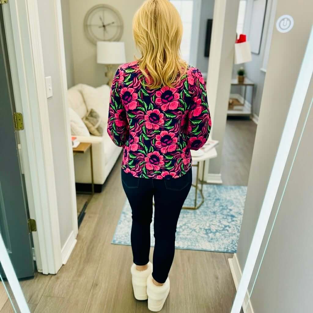 Woman wearing the SIENNA LOVESTRUCK TOP by Michelle McDowell, featuring a vibrant pink floral print, styled with dark jeans.