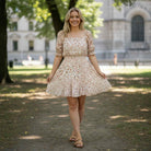 Model wearing RUSTIC GRACE by Trixxi, a soft orange floral mini dress in a sunny outdoor setting.