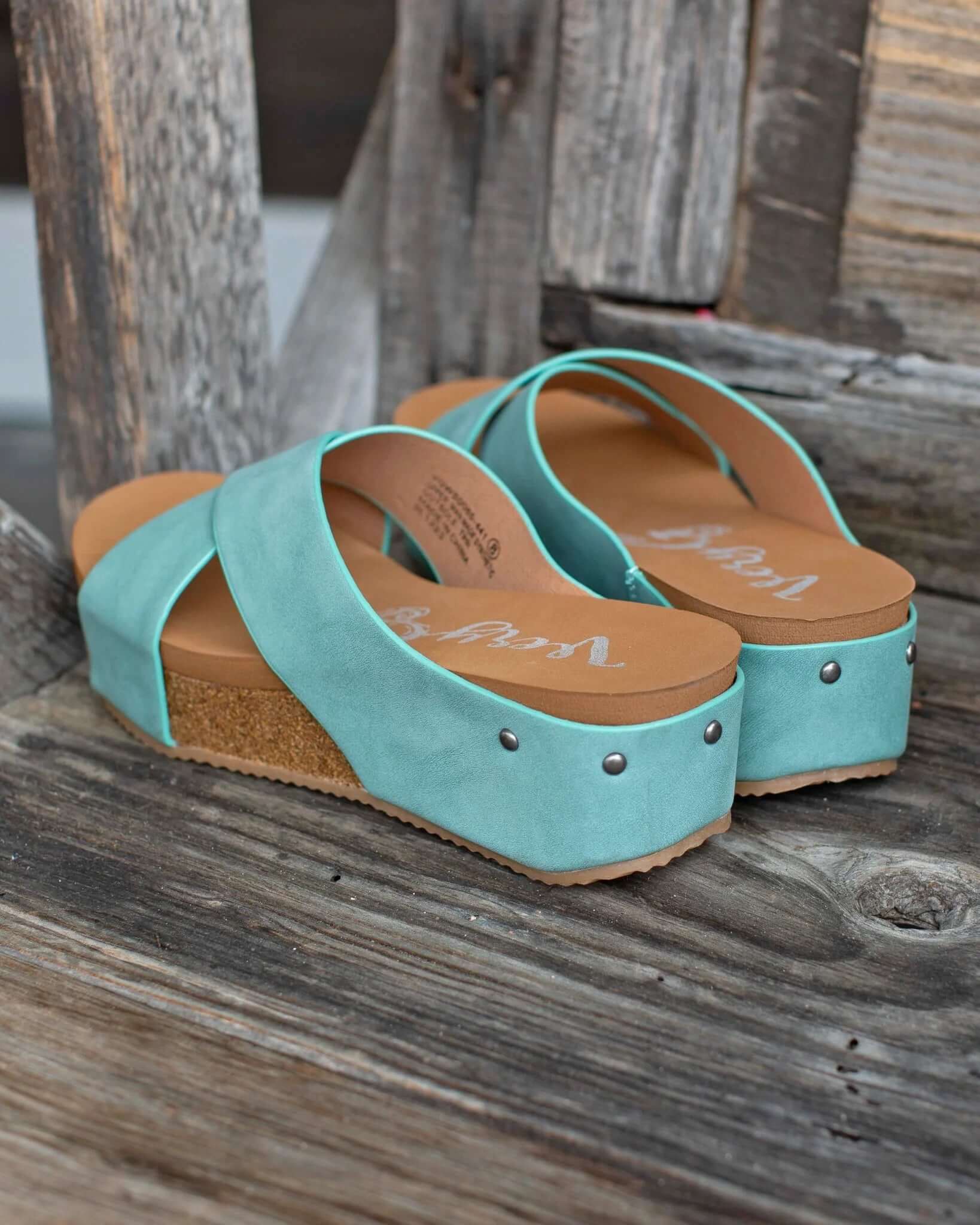 Teal platform wedge sandals by Very G with distressed faux leather straps and studded details on a wooden surface.