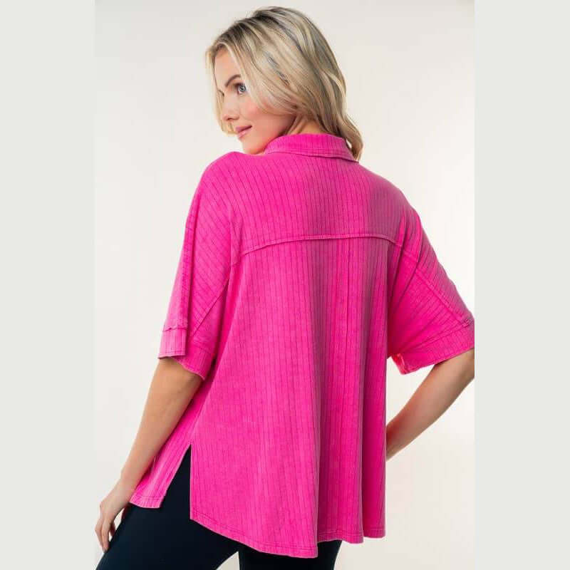 Back view of a woman in a hot pink ribbed knit collared top with half sleeves and side slits.