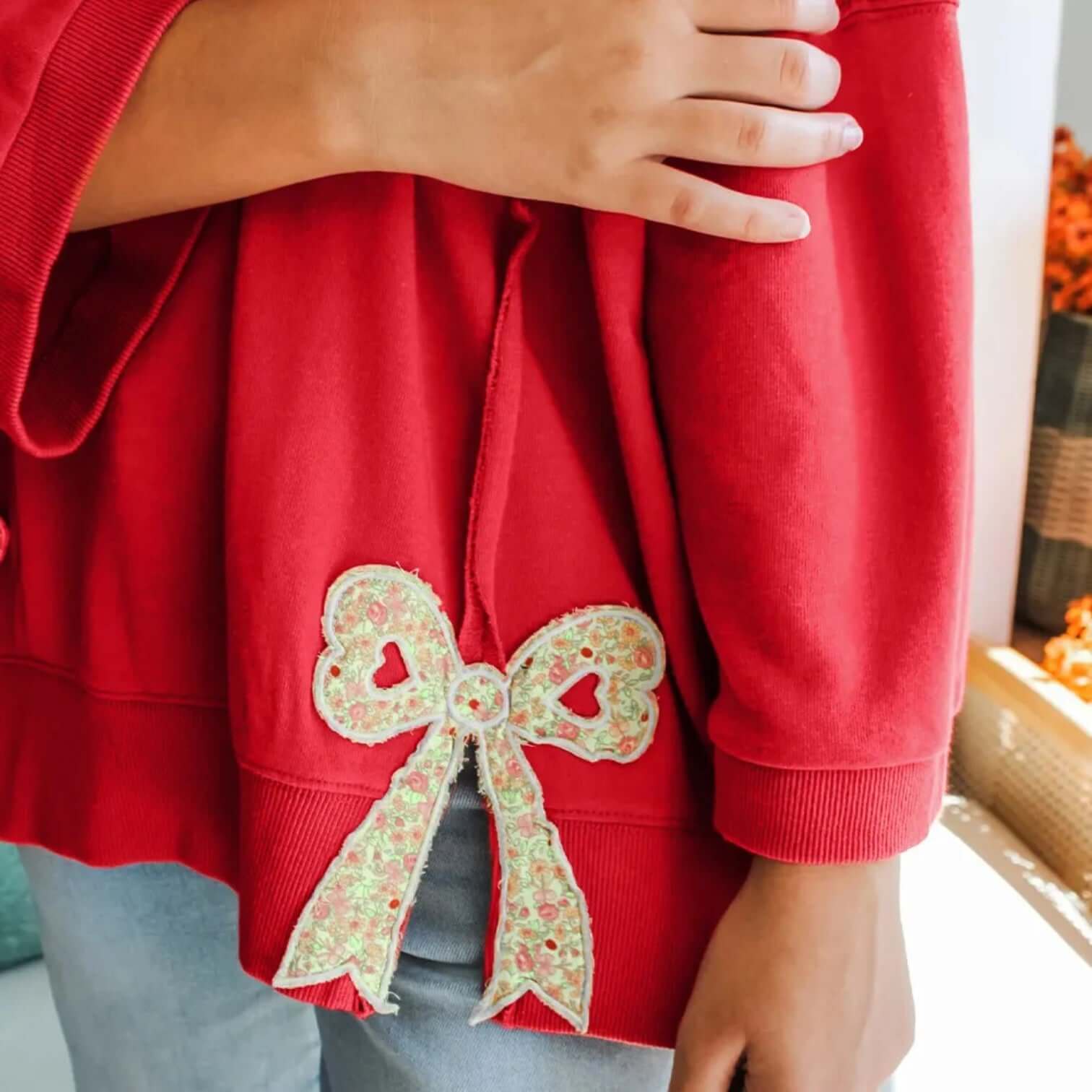 SWEETHEART BOW TOP (red) with floral bow patch detail on a relaxed sweatshirt showcasing feminine charm.