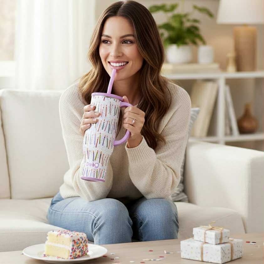 Woman enjoying her MAKE A WISH 30 oz - SWIG mug with confetti design while sitting on a couch.