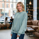 DOWNTOWN DRIFT CREW NECK worn by a smiling woman in a cozy cafe setting, showcasing its mineral wash finish.