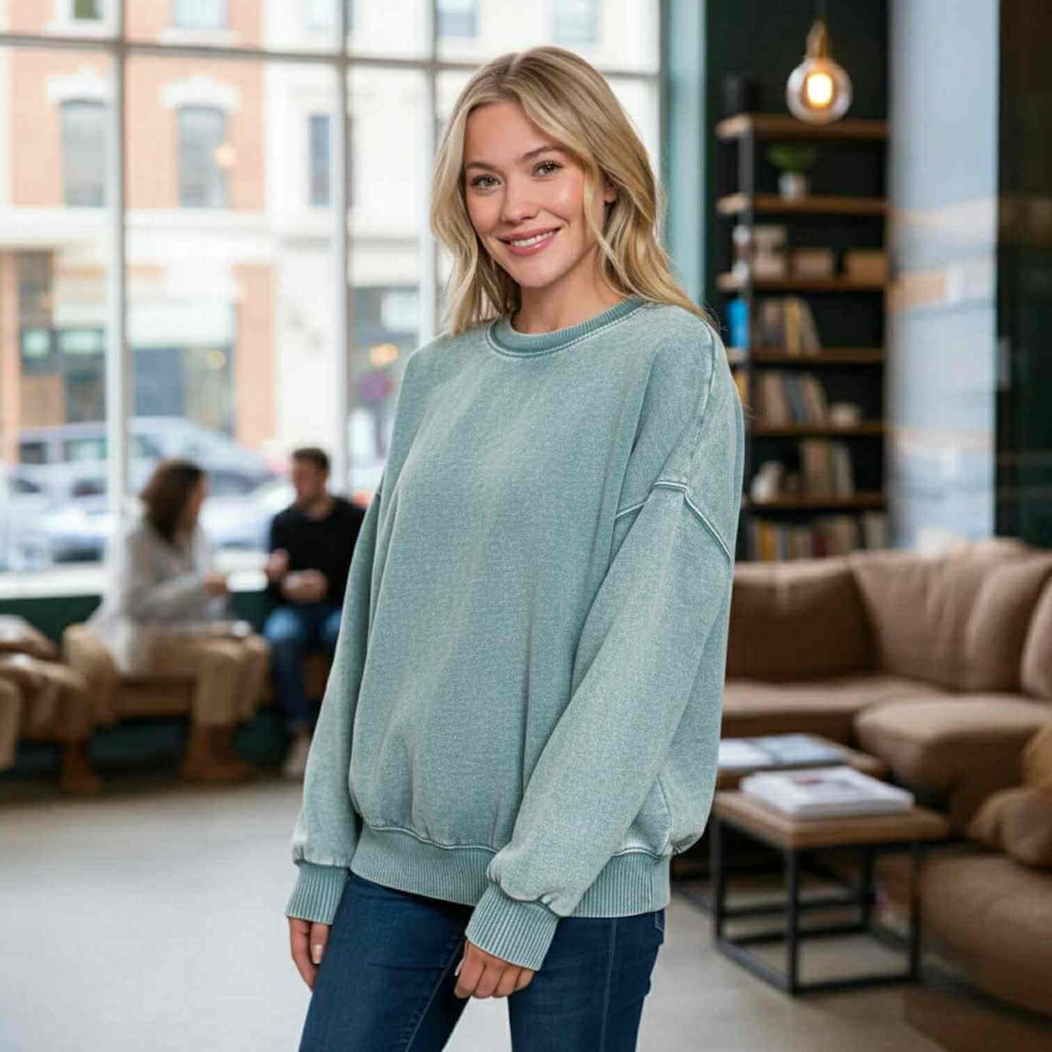 DOWNTOWN DRIFT CREW NECK worn by a smiling woman in a cozy cafe setting, showcasing its mineral wash finish.