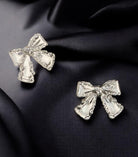 SILVER BOW Stud Earrings from Vivian-Lu collection, featuring elegant design on a dark fabric background.