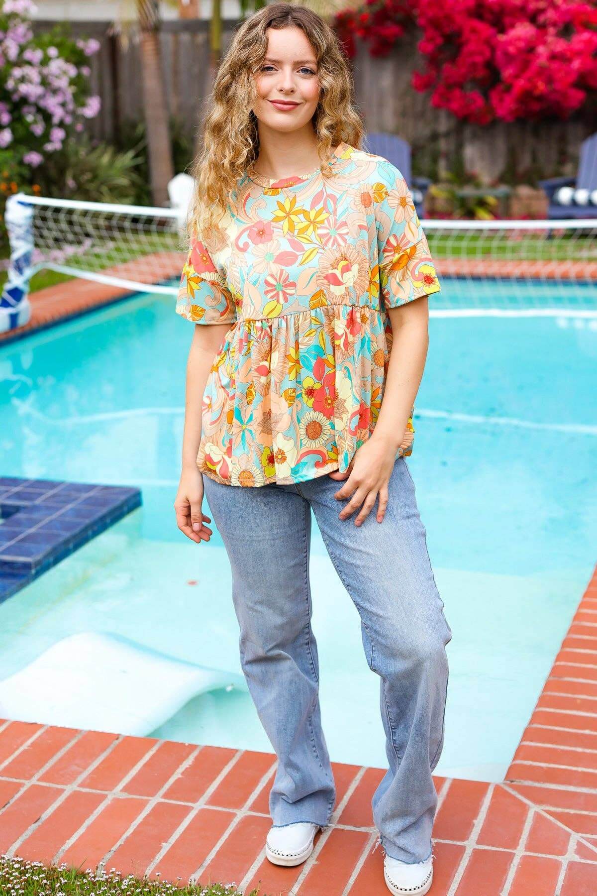 Woman wearing Retro Romance Top by Haptics, floral peplum style, near a swimming pool with vibrant pink flowers.