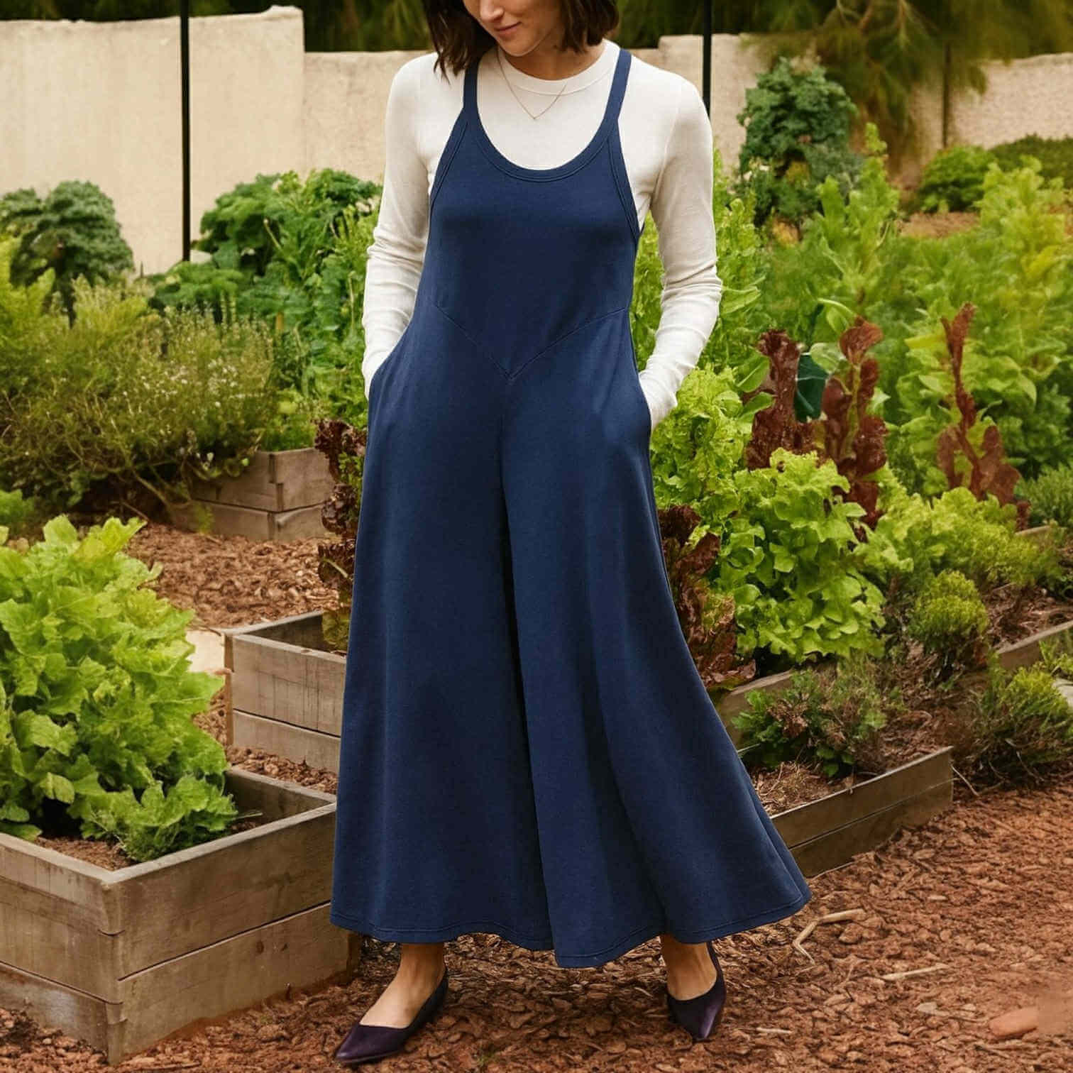 Model wearing EVERY DAY ESCAPE JUMPSUIT in a garden, showcasing its flowy wide-leg silhouette and keyhole back.