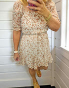 Woman wearing RUSTIC GRACE by Trixxi mini dress with floral print and smocked waist, styled for a chic summer look.