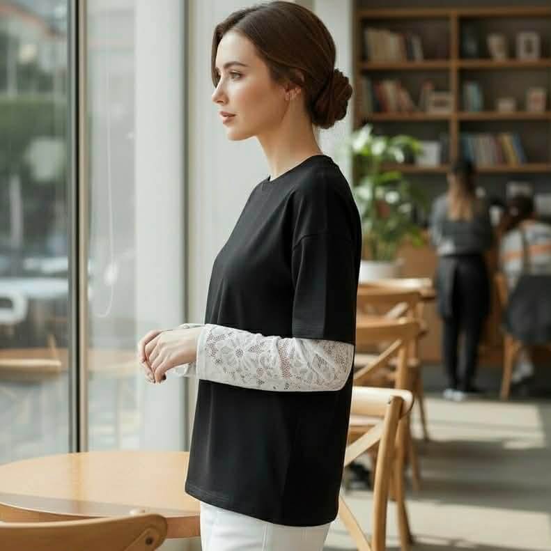 Model wearing COFFEE & CREAM TOP black tee with lace long sleeve inserts in a cafe setting.