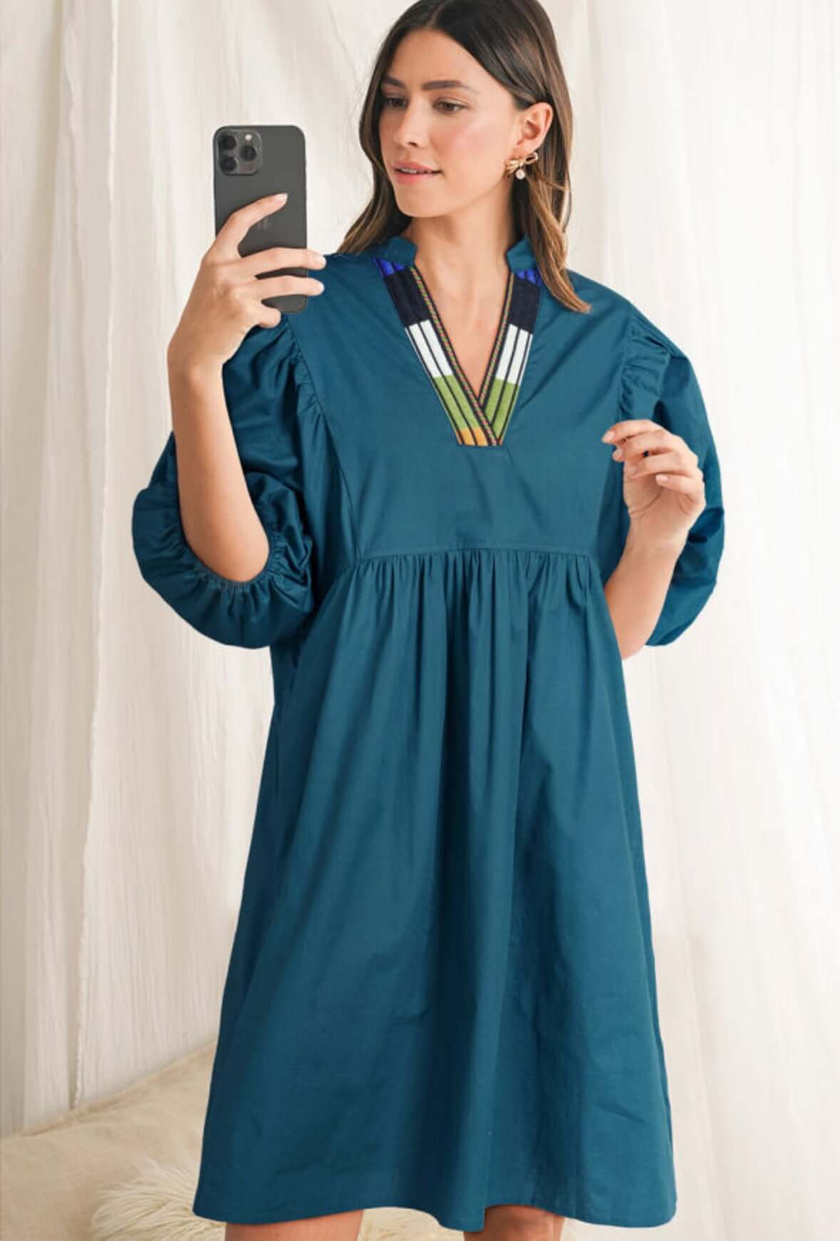 Woman wearing the Aurora Dawn Dress in teal with colorful embroidered neckline and puff sleeves.