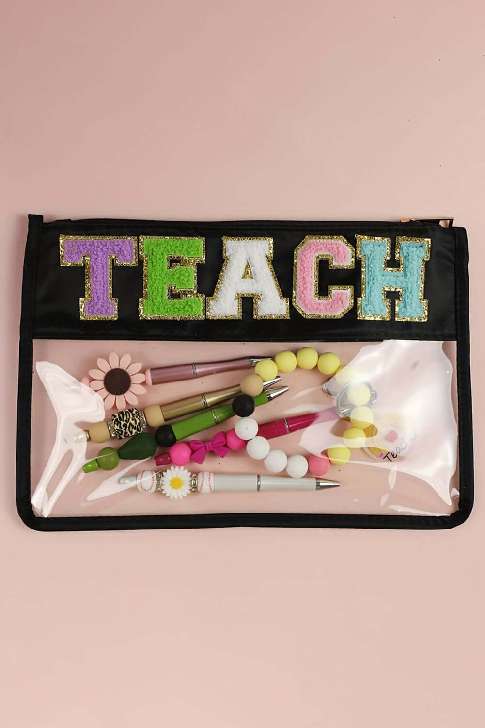 In My Teacher Era clear zipper pouch featuring glitter lettering 'TEACH' on a black background, filled with colorful pens.