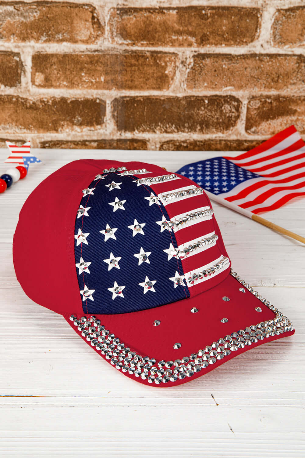 Red baseball cap featuring American flag print and rhinestones, perfect for patriotic occasions.