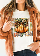 Woman wearing a cozy jacket showcasing the PUMPKIN PARTY TEE with a decorative pumpkin and bow design.