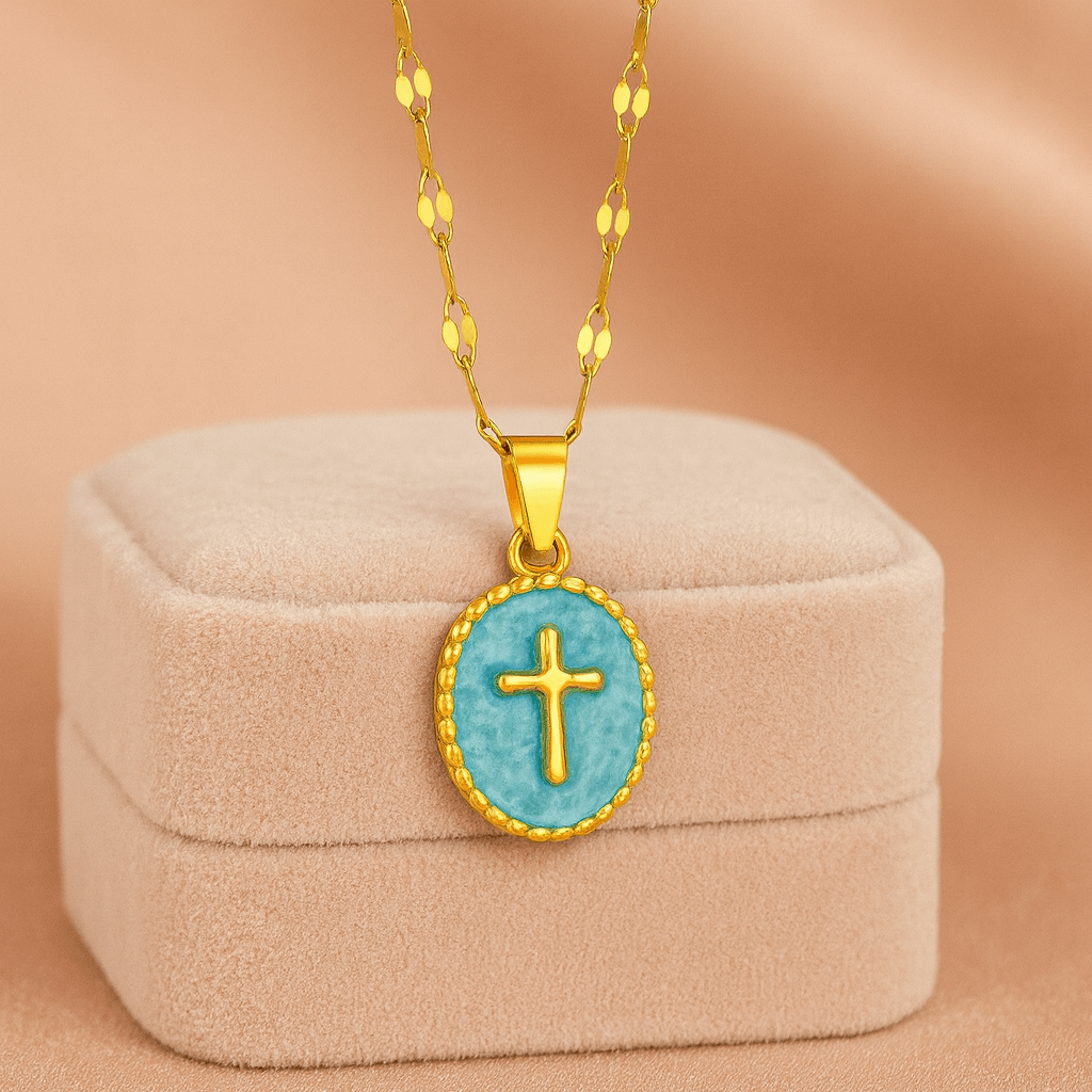 Gold-tone cross pendant necklace with teal enamel on velvet display.