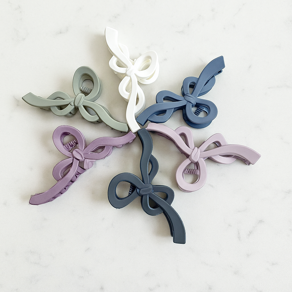 Six colorful matte bow claw clips in shades of green, gray, blue, and purple on a marble surface.