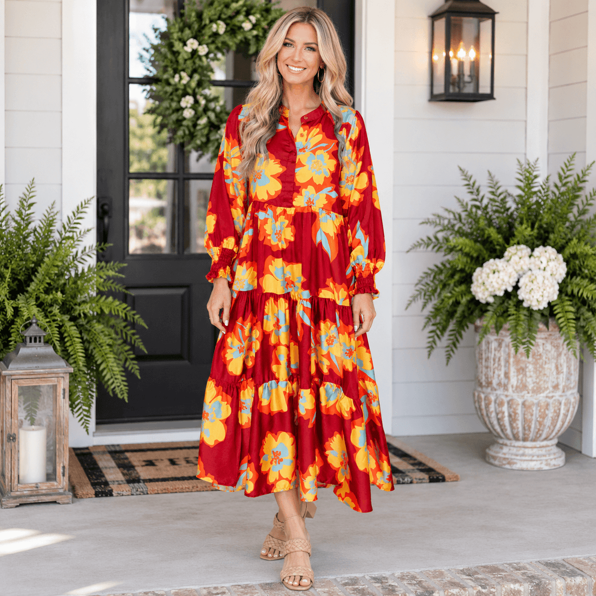 Model wearing the vibrant SOUL FIRE DRESS featuring floral patterns in red and yellow, standing on a porch.
